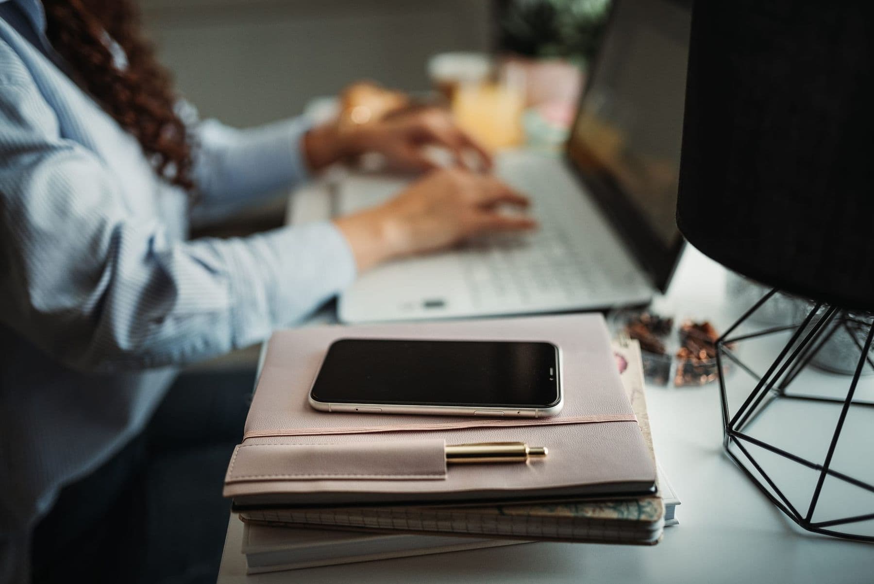 Person typing on a laptop with notebooks and a smartphone on the desk