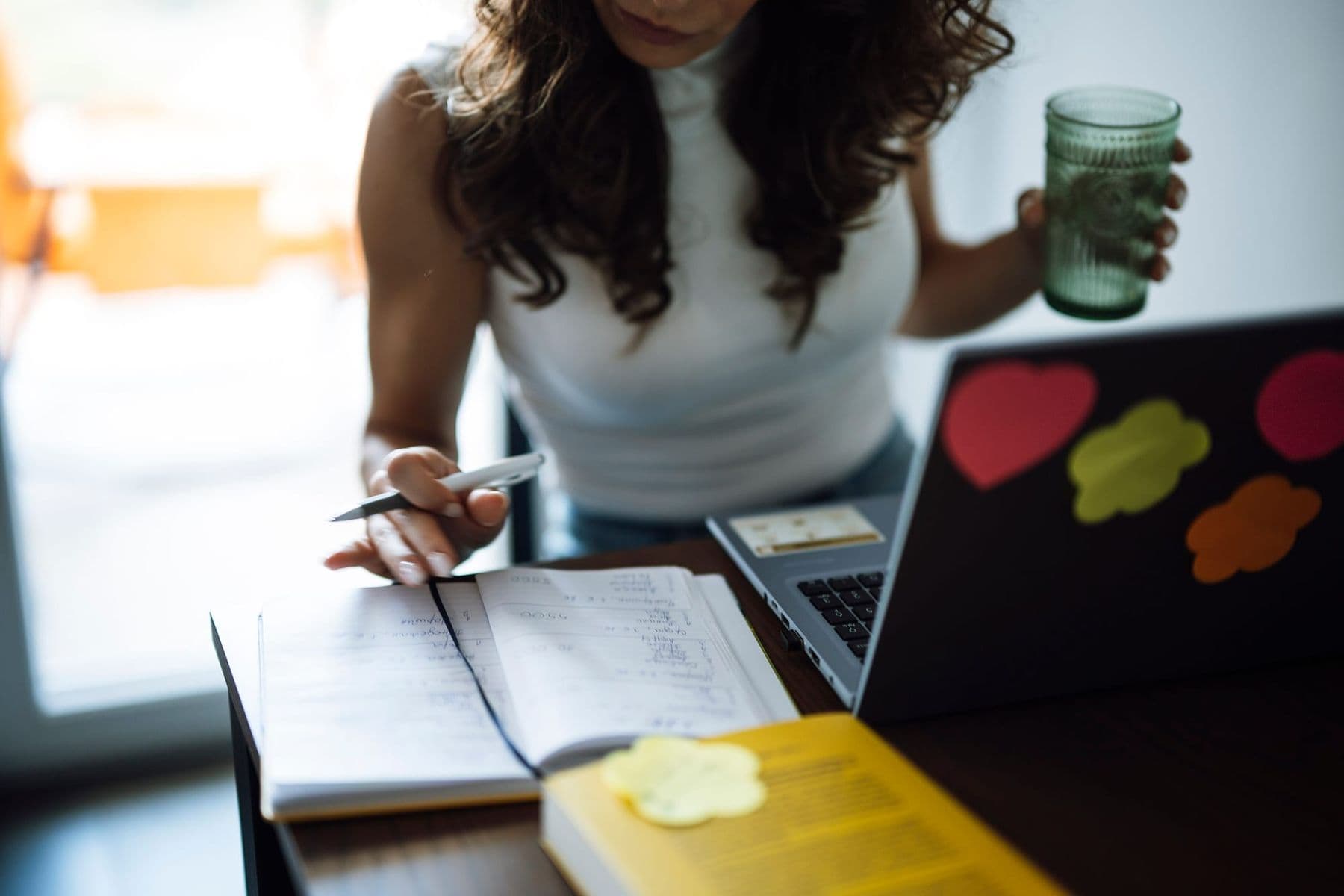 Woman writes in a notebook beside a laptop, planning a lesson with AI in education