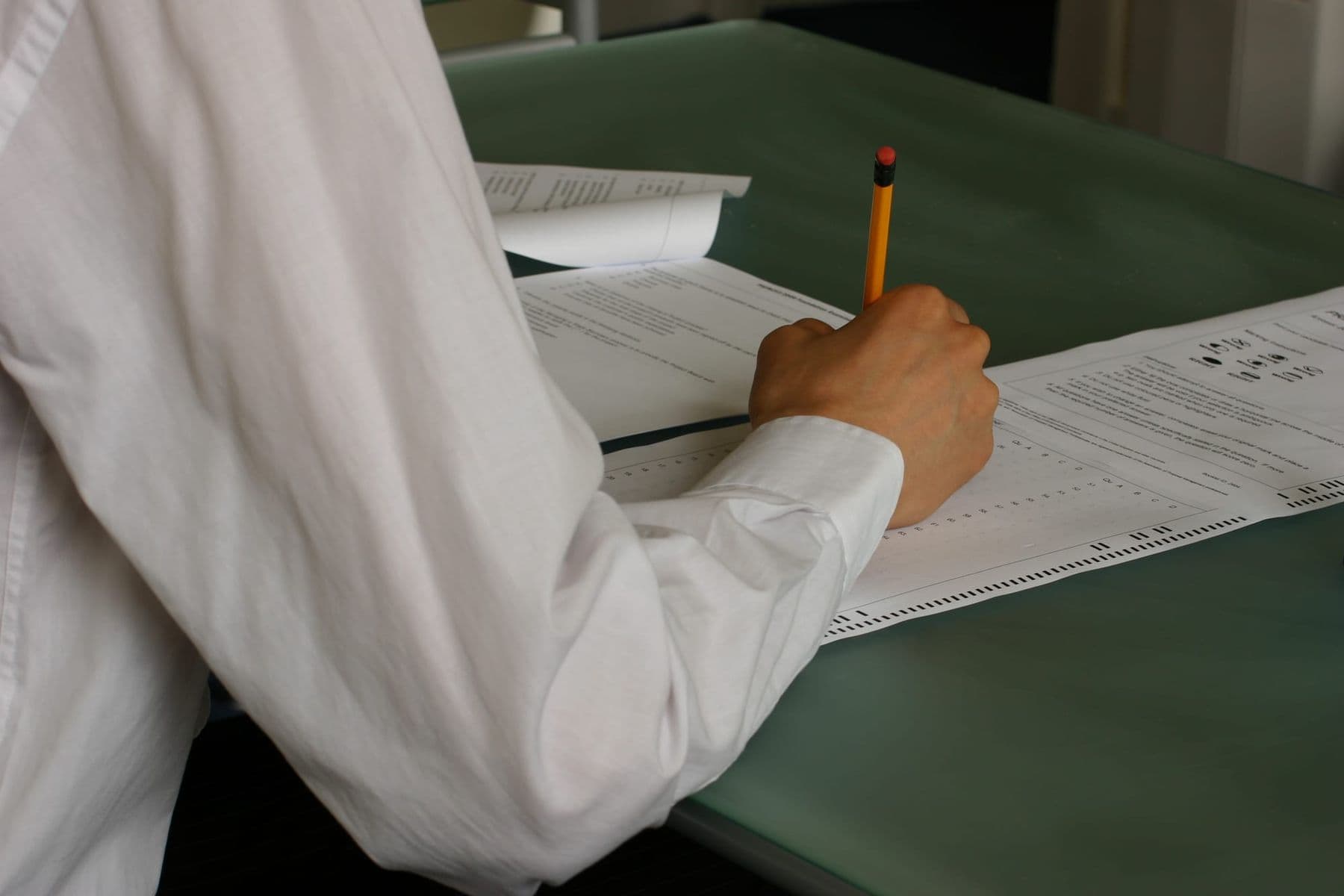 A student's hand fills in an exam answer sheet with a pencil