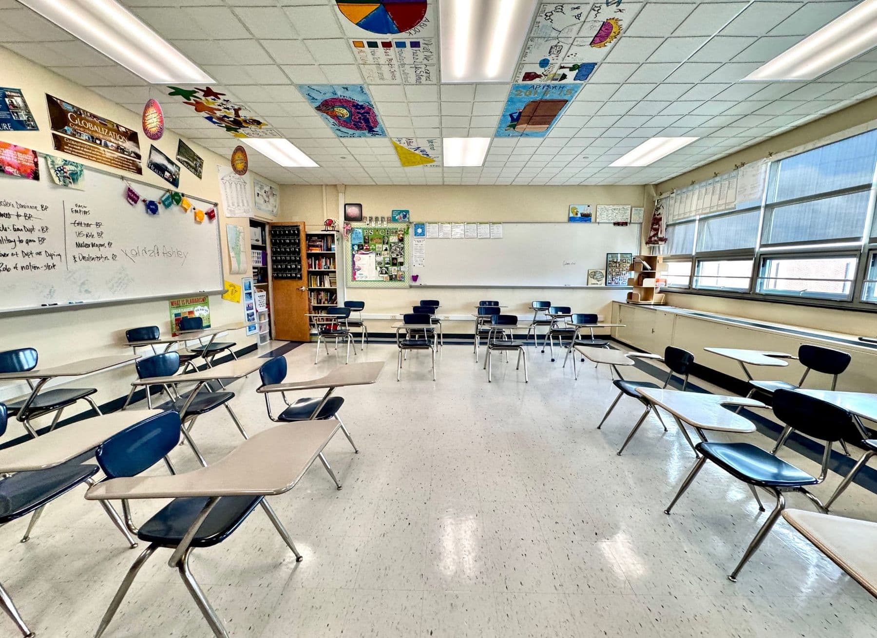 Bright empty classroom with student desks, whiteboards and a bookshelf