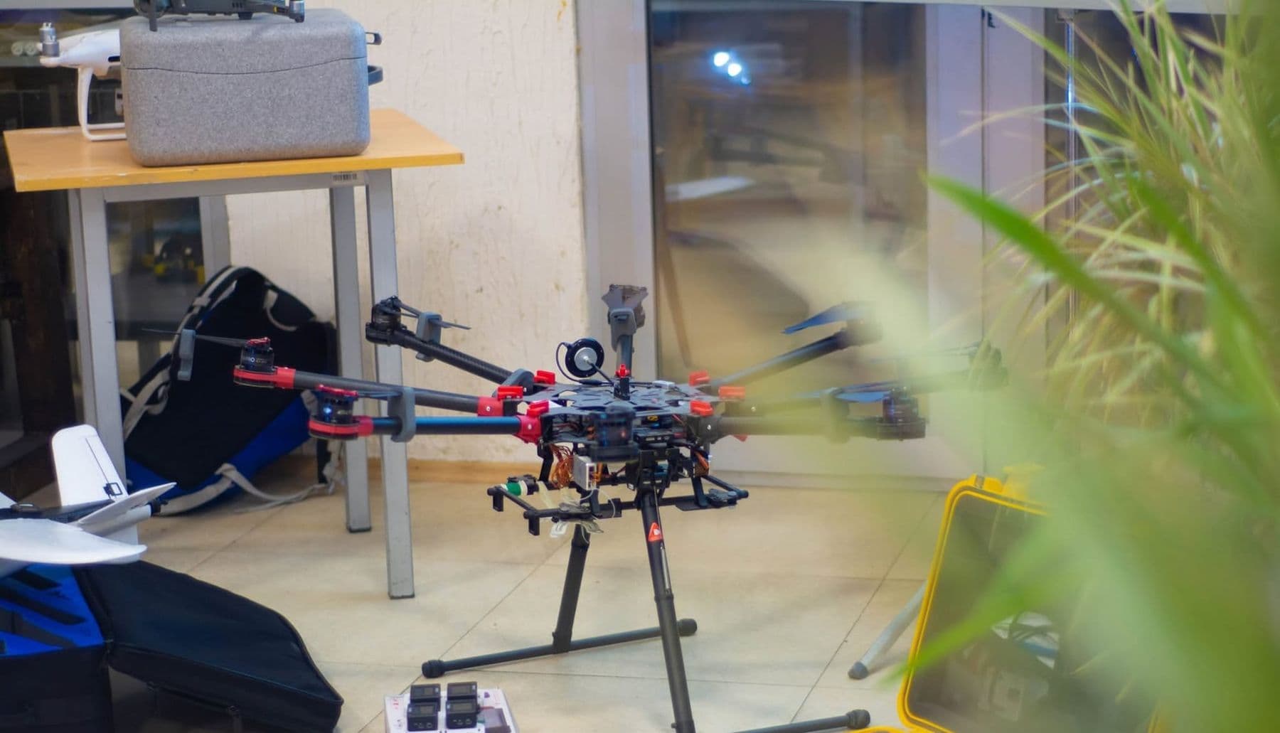A large six-rotor drone on the floor beside cases and a fixed-wing drone