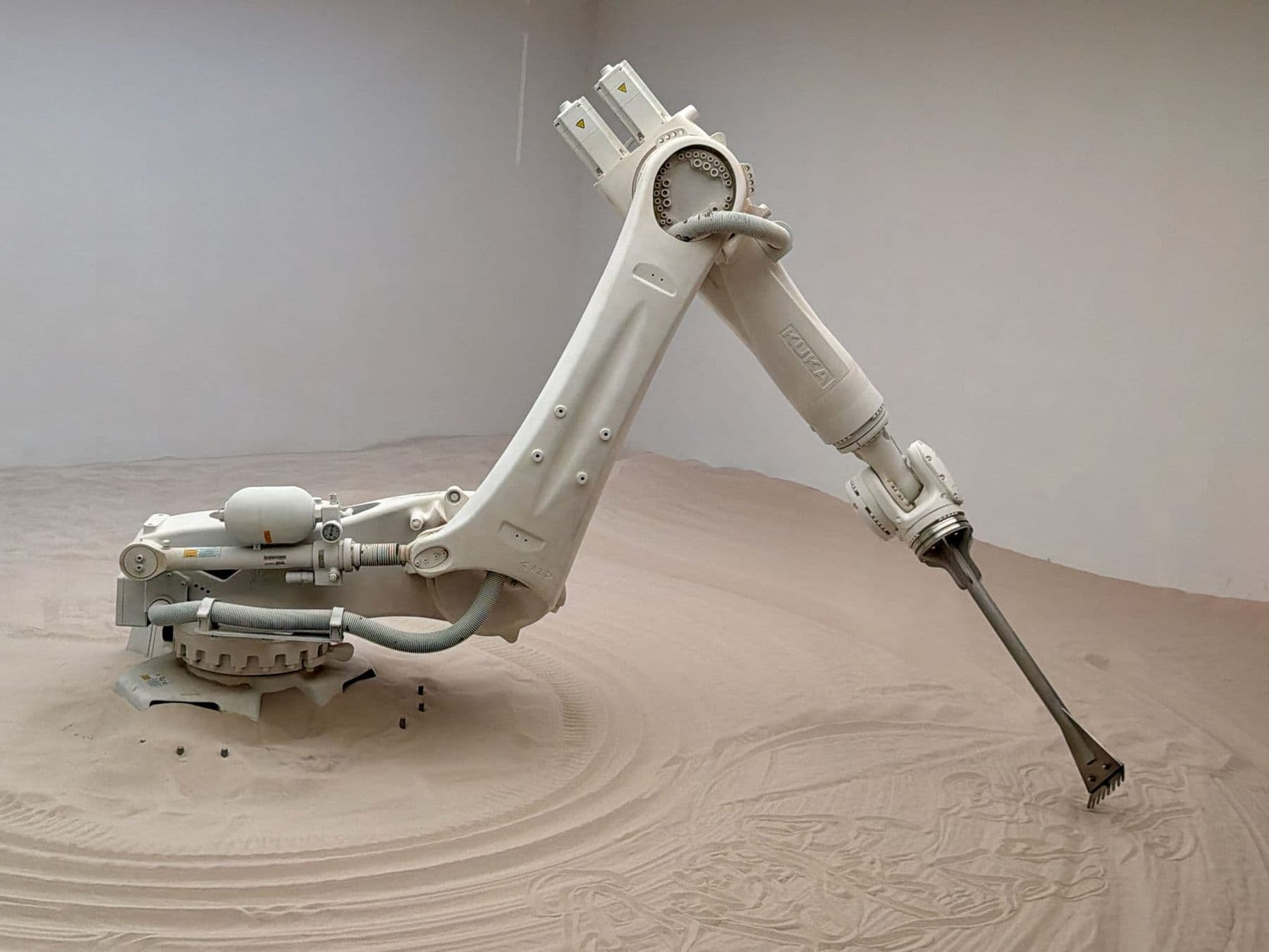 White industrial robotic arm drawing patterns in sand