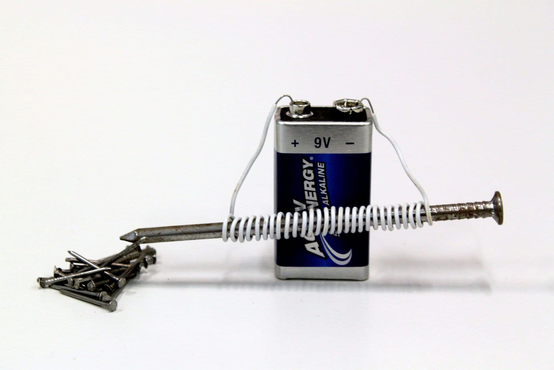 Homemade electromagnet: wire coiled on a nail connected to a battery, small nails