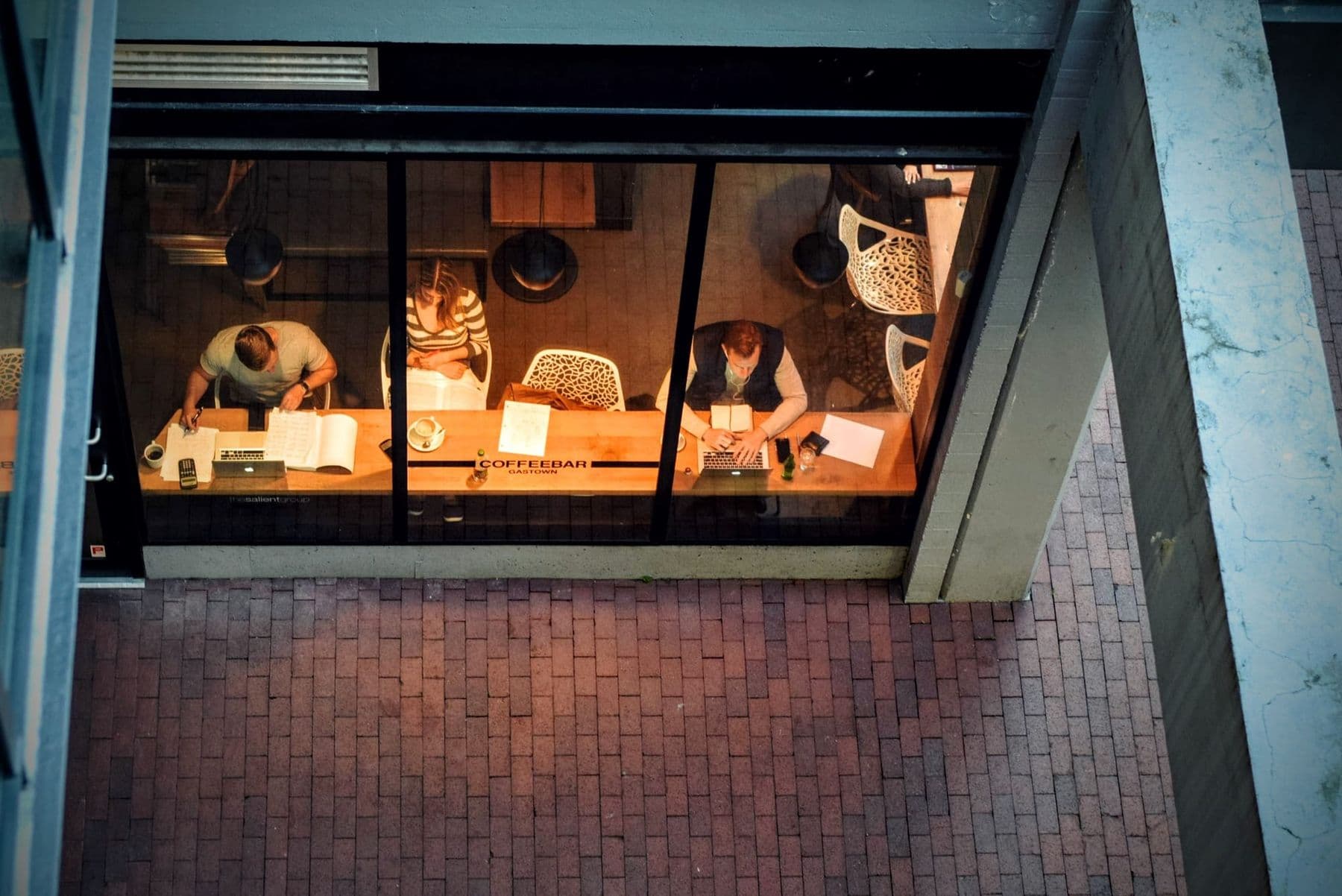 People work with laptops and books in a café, seen from above through a window