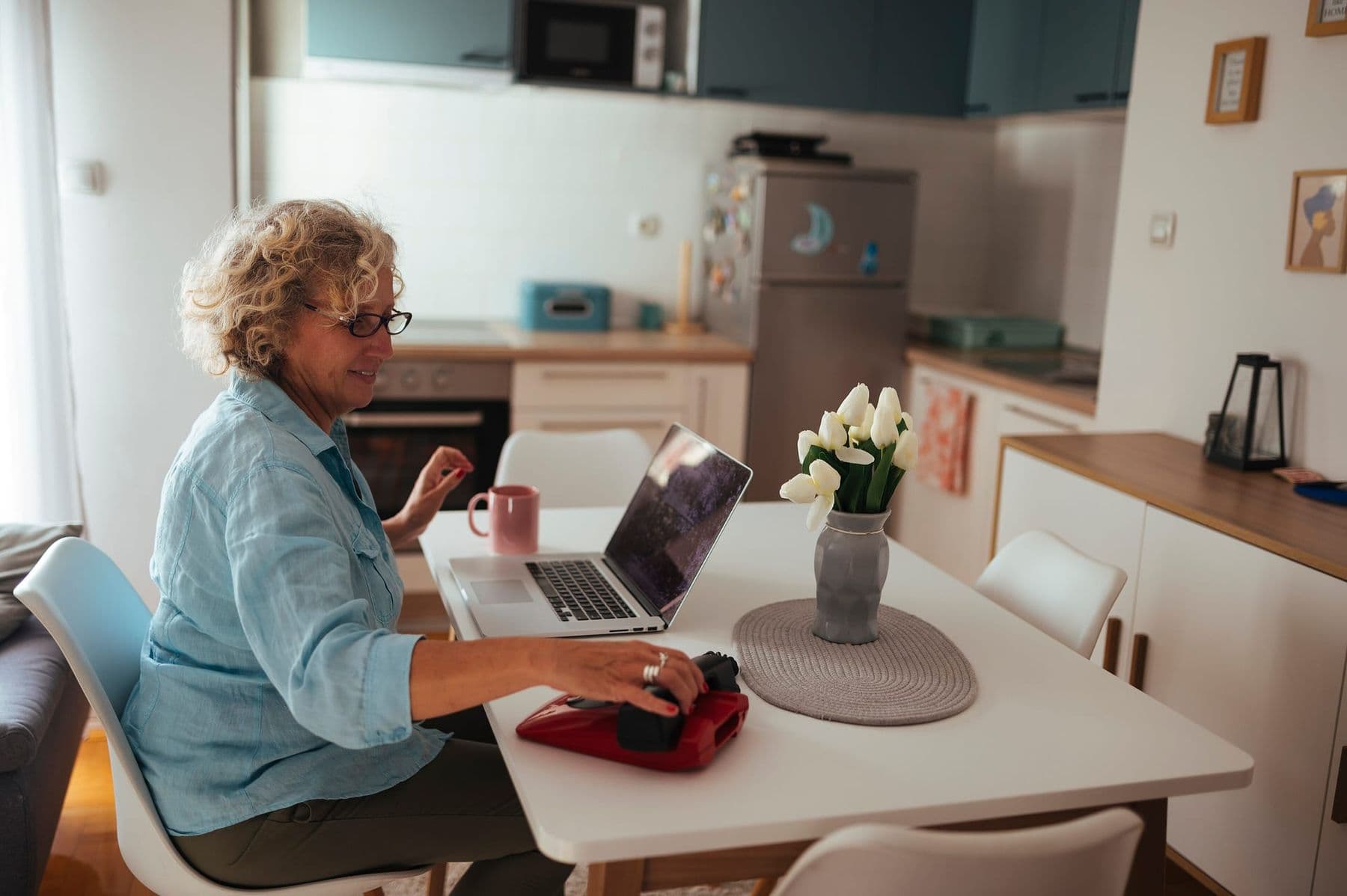 Senior woman smiling while using a laptop at her kitchen table