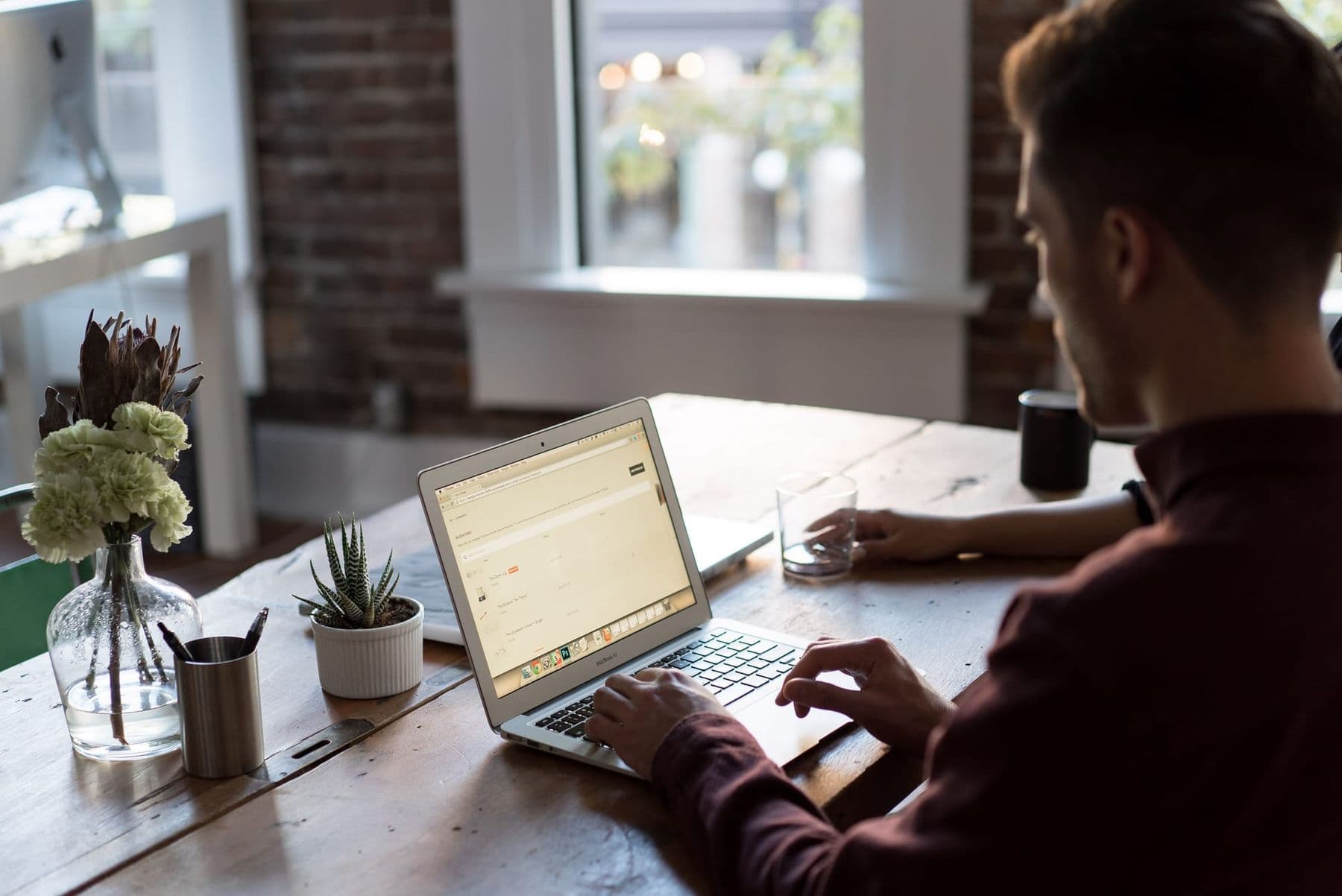 Man working on a laptop at a wooden desk by the window