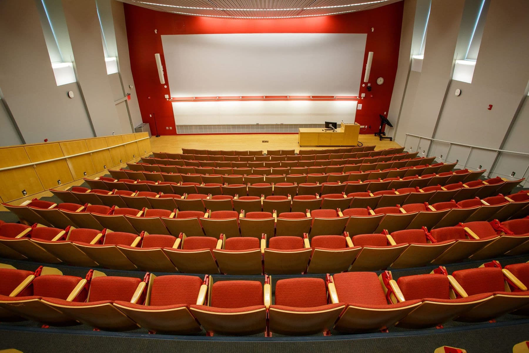 Large university lecture hall with red seats and a projection screen