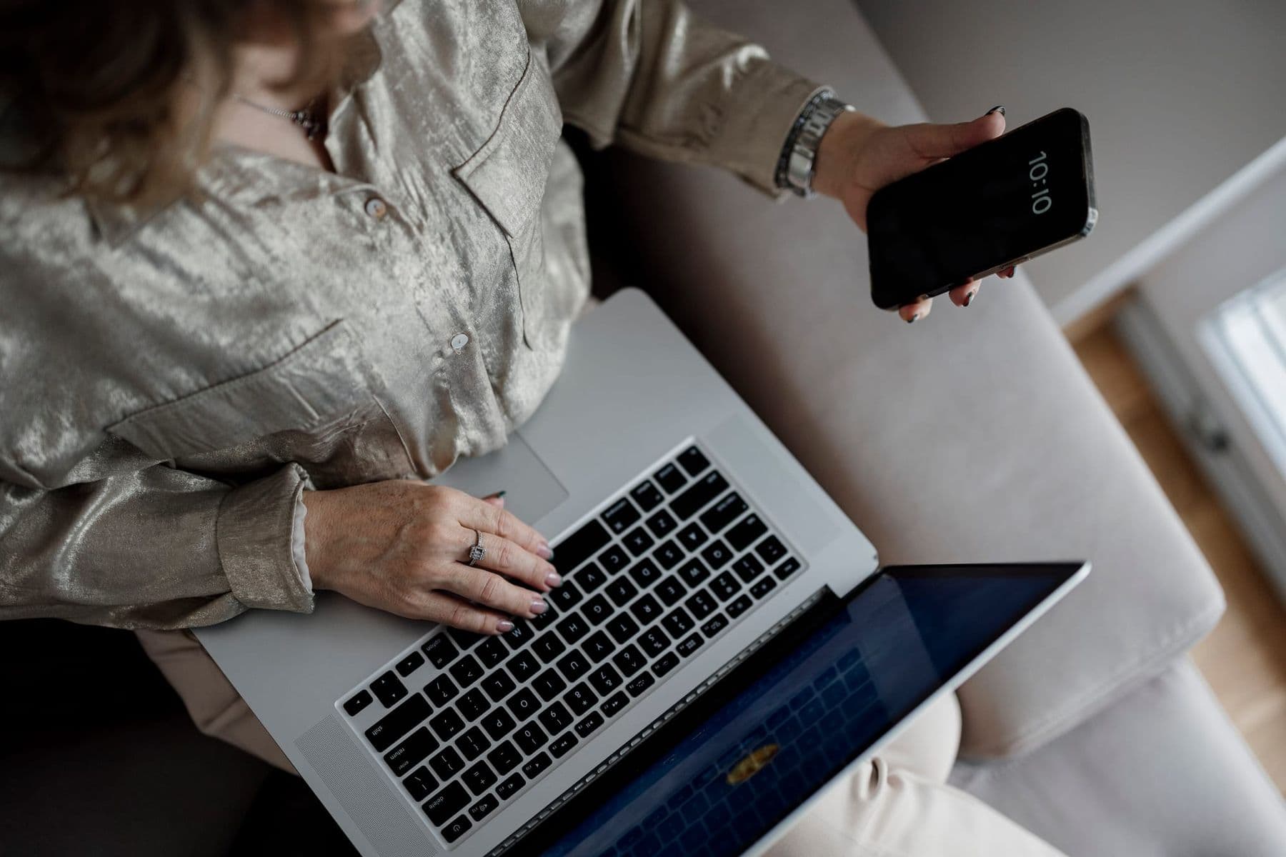 A woman types on a laptop while holding a smartphone, using ChatGPT on both devices