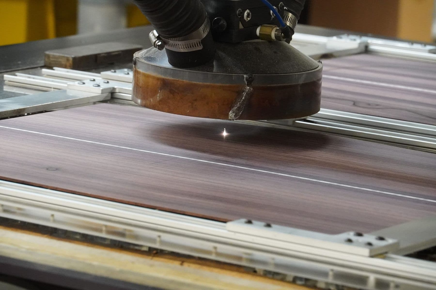 A laser cutting head slicing a thin wood veneer sheet, with a bright spark at the cut