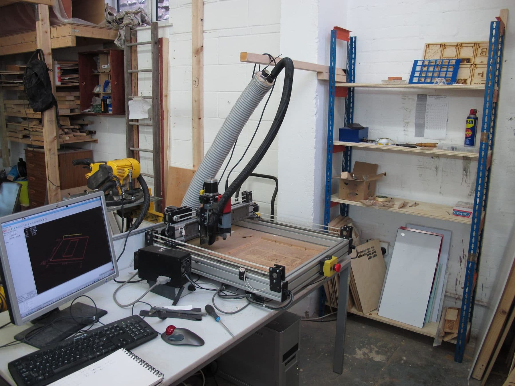 Desktop CNC router in a workshop next to a computer showing a drawing