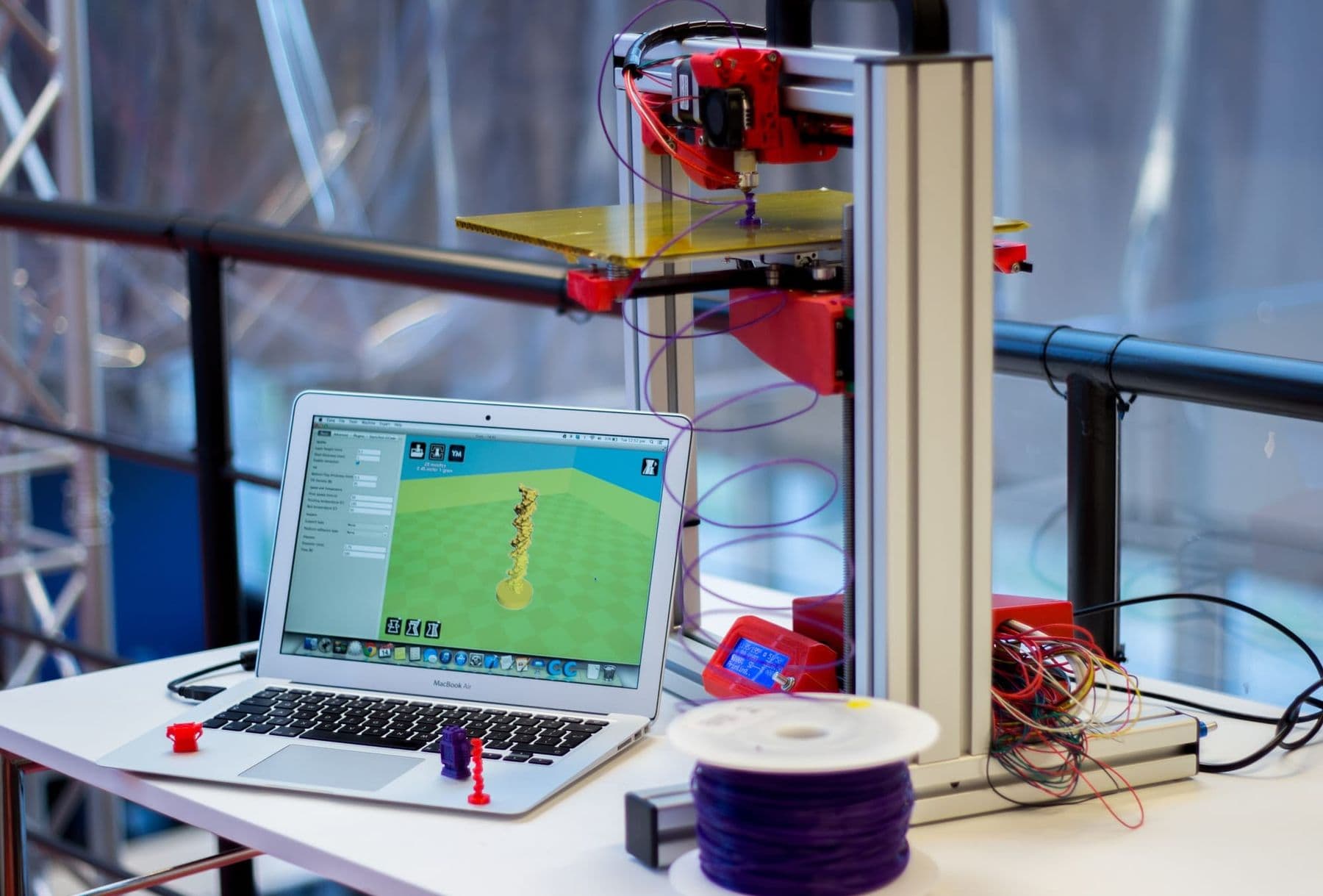 Laptop running slicer software next to a 3D printer and filament spool
