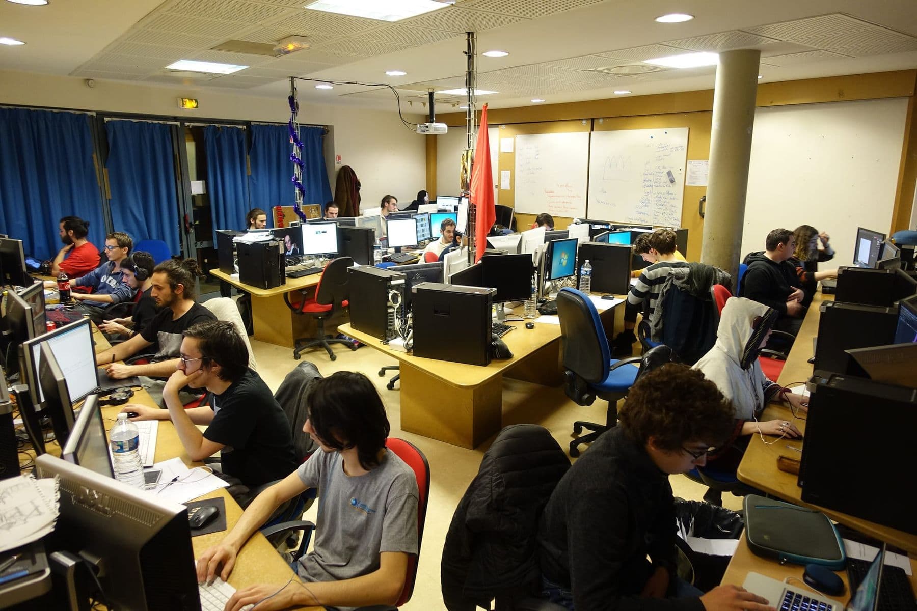 Global Game Jam-ის მონაწილეები კომპიუტერებთან თამაშებს ქმნიან დიდ საკლასო ოთახში