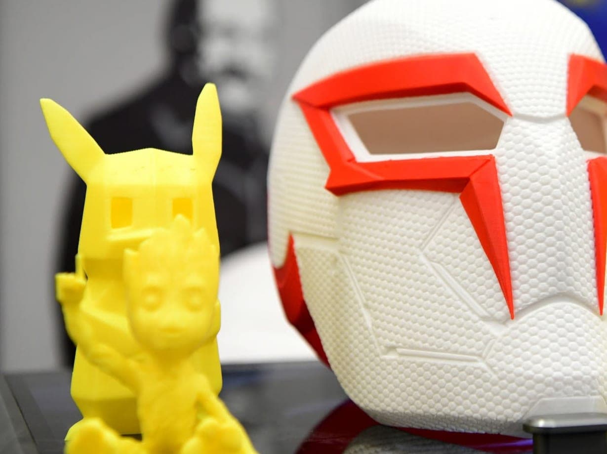 A white 3D-printed helmet with red details beside a yellow printed figurine
