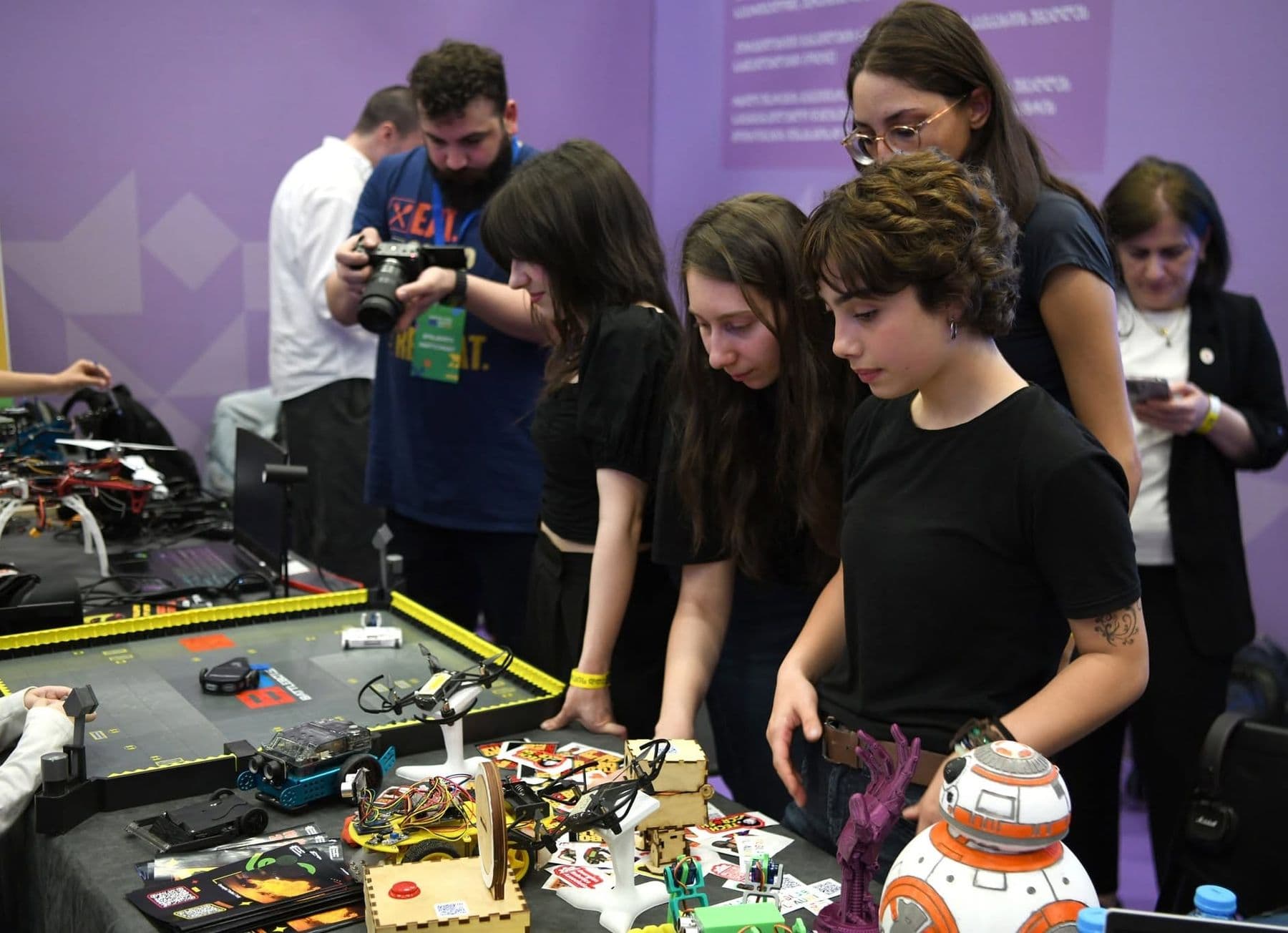 Teenagers lean over a table of small robots and a practice track mat