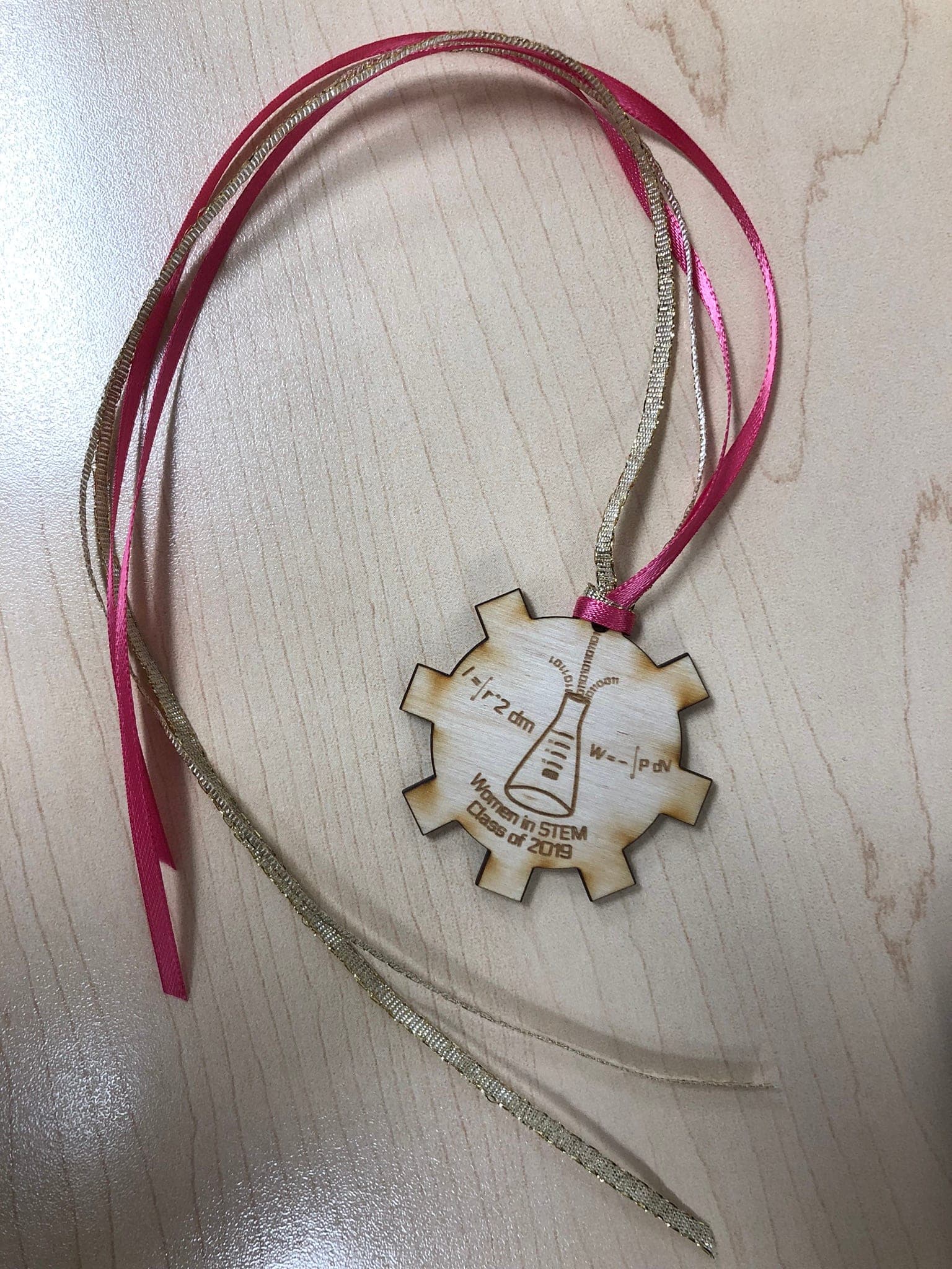 A laser-cut and engraved wooden medallion with lettering and ribbons