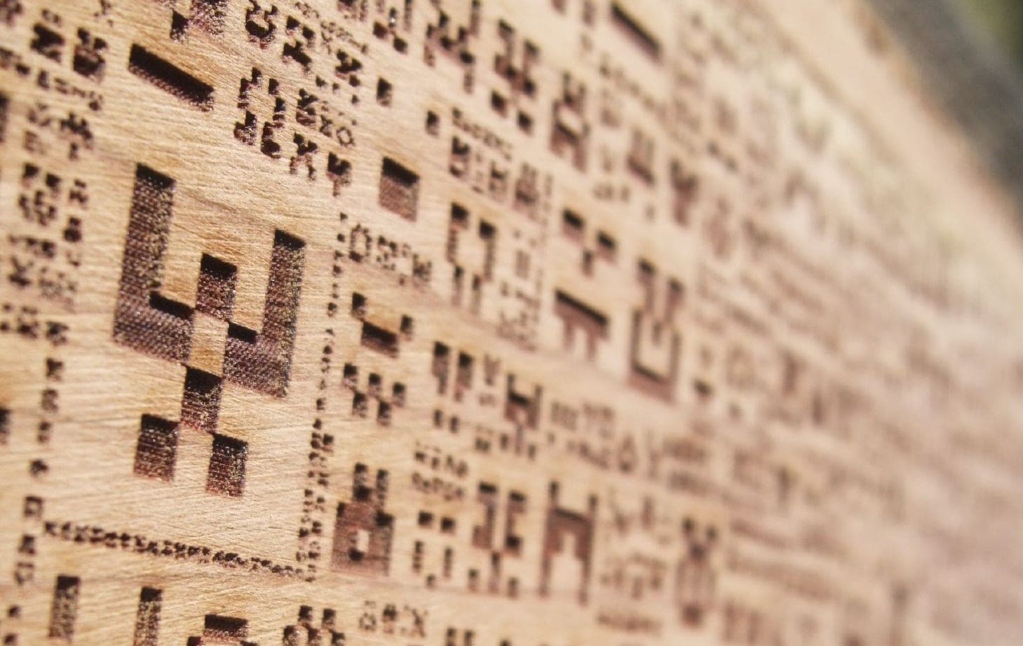 Close-up of pixel-art figures laser engraved into a wooden board