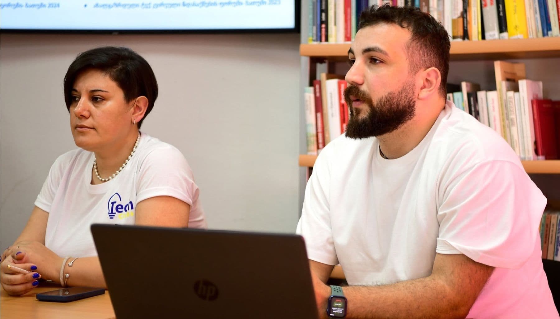 A training session in a library: two participants at a laptop listen and talk